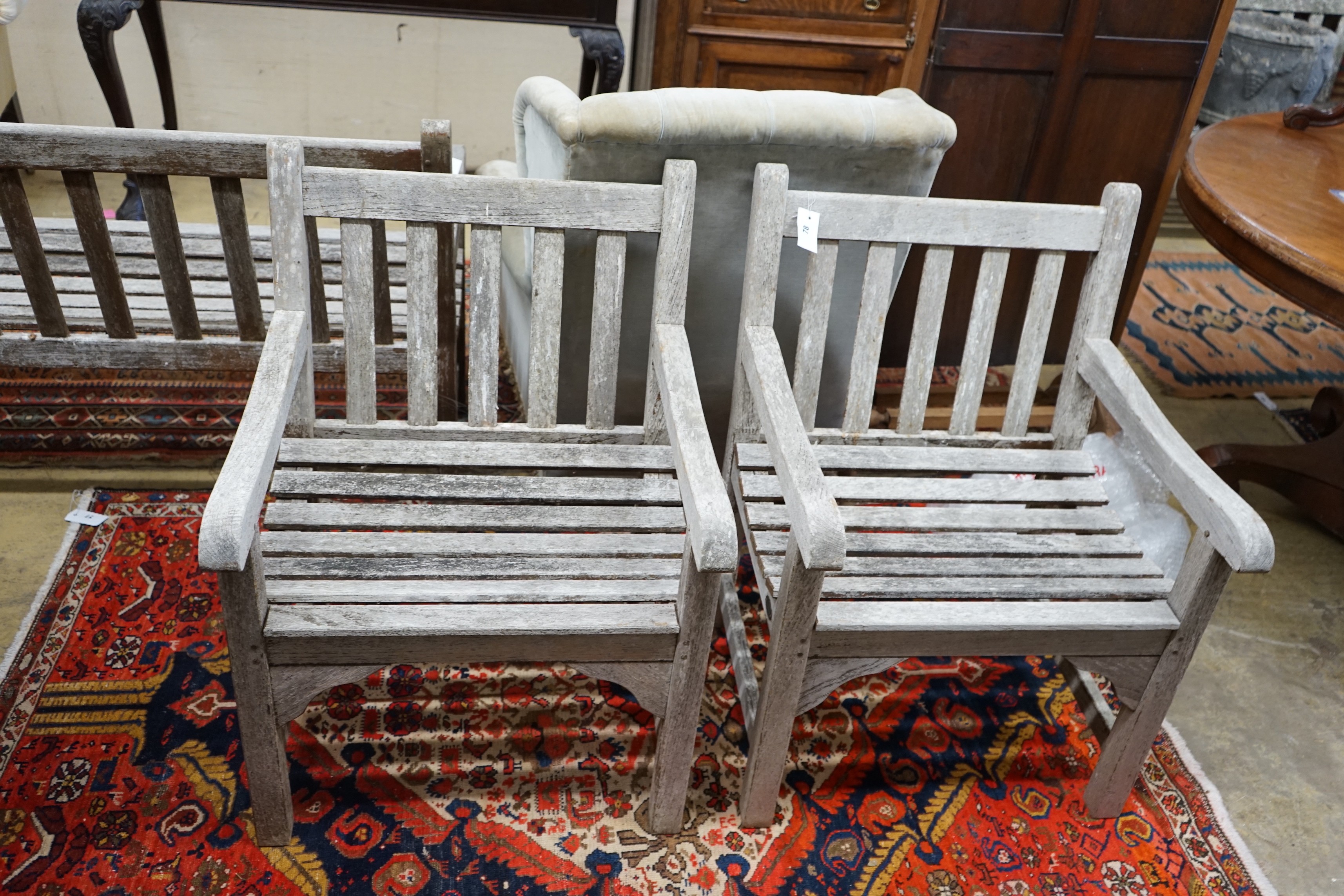 A pair of slatted weathered teak garden elbow chairs, width 60cm, depth 58cm, height 83cm